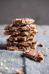 Thin chocolate bark topped with nuts, quinoa and seeds, broken into rustic pieces.